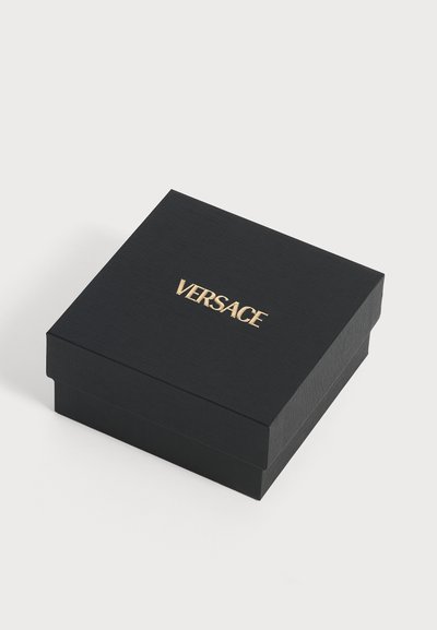 Boîte carrée noire texturée avec le logo VERSACE doré centré sur le couvercle, présentée sur un fond blanc uni.