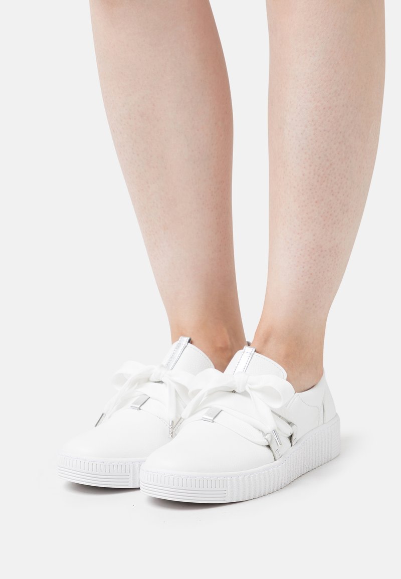 Sneaker bianchi con suola in gomma testurizzata, ampie stringhe bianche e dettagli in metallo argentato, caratterizzati da una finitura liscia e una punta arrotondata.