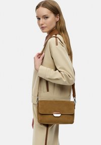 Borsa a tracolla in suede tan con chiusura a pattina, caratterizzata da un accento in metallo argento e una tracolla marrone a contrasto. Design semplice e rettangolare.