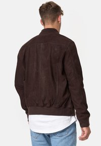 Braune Wildleder-Bomberjacke mit gerippten Bündchen und Kragen, die eine glatte Textur und eine taillierte Passform für eine schlanke Silhouette aufweist.