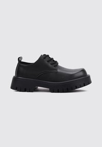 Zapatos de cuero negro con cordones, punta redondeada y suela gruesa y texturizada. Presentan un pequeño lazo trasero para facilitar el calzado.