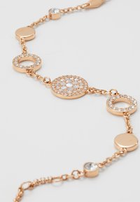 Bracciale in oro rosa con anelli circolari, alternando lisci ed embellished con cristalli trasparenti, centro decorativo intricato.