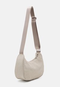 Sac à épaule en tissu beige avec une forme incurvée, fermeture éclair et bandoulière beige réglable, présentant une texture lisse et un design minimaliste.