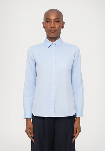Chemise bleu clair à col pointu, à manches longues, avec une poche poitrine unique et un ourlet arrondi, fabriquée à partir d'un tissu lisse.