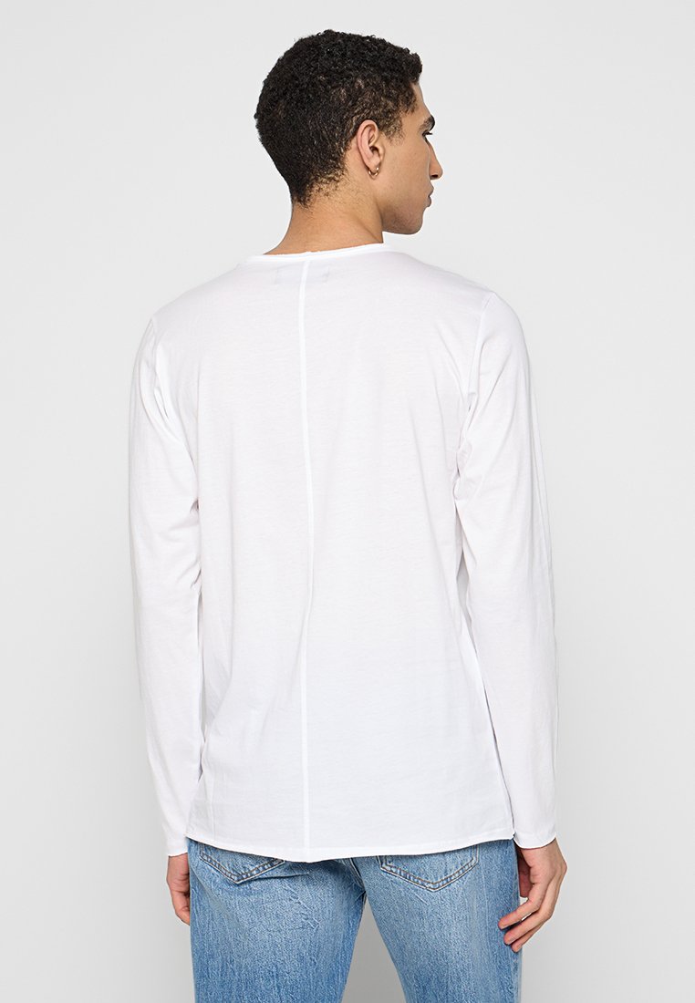 Camiseta de manga larga blanca hecha de algodón suave, con un dobladillo recto y un detalle de costura en la parte de atrás, combinada con unos jeans de mezclilla azul claro.