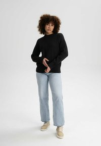 Schwarzer gerippter Pullover mit Rundhalsausschnitt, langen Ärmeln und enganliegenden Bündchen, kombiniert mit hellblauen geraden Jeans und beigen Sneakers.