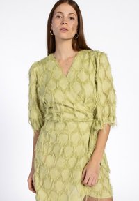 Hellgrünes Kleid mit strukturiertem, fransigem Muster. Hat einen V-Ausschnitt, kurze Puffärmel und ein Wickeldesign, das an der Taille betont.