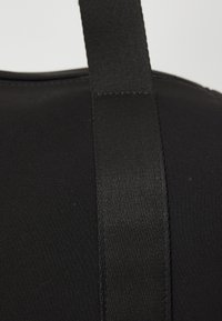 Bolsa de tela negra con una textura suave y una correa ancha y plana. El material es ligeramente brillante y presenta costuras a lo largo de los bordes.
