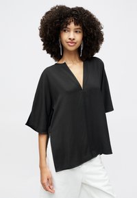 Sort, kortærmet top med V-hals, der har en afslappet pasform, sideslidser og en glat tekstur. Sammen med hvide bukser.