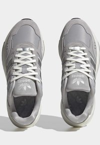 Ett par grå Adidas-sneakers med vita snören, ovandel av mocka och mesh, synlig logotyp på tungan och mönstrade innersulor, visade uppifrån.