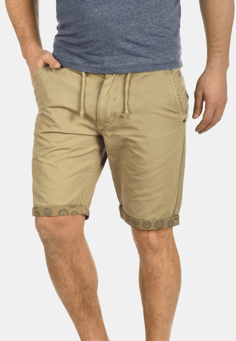 Pantalones cortos de algodón beige con cintura elástica y puños doblados, que presentan un diseño floral a lo largo de los dobladillos. Ligero y de corte casual.