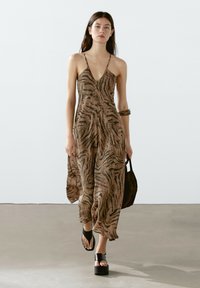 Robe rayée marron et noire avec un décolleté en V plongeant, des bretelles spaghetti et une silhouette fluide. Assortie à des sandales à plateforme noires et un sac.