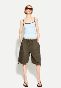 Light blue fitted tank top with black trim, paired with olive cargo shorts featuring two large side pockets and a drawstring waist. Black flip-flops.