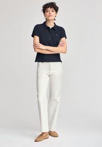 Marinblå pikétröja med korta ärmar och fem knappar, kombinerad med vita raka byxor och ljusbruna loafers. Enkel, strukturerad design.