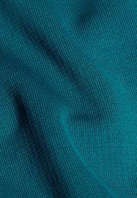 Tessuto smeraldo a coste che mostra una trama liscia e pieghe morbide, presenta un motivo coerente con lievi variazioni di tonalità e profondità.