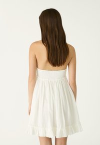 Weißes Sommerkleid mit einem gerafften Oberteil und einem fließenden Rock mit einem Rüschensaum. Der Stoff wirkt leicht und leicht strukturiert.