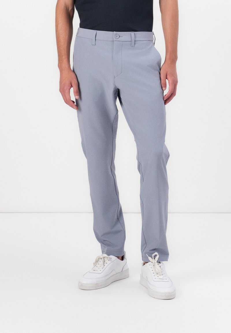 Hallid slim-fit püksid sujuva tekstuuriga, lukuga, nupuga kinnitamise ja peente küljetaskutega, koos valgete tossudega.