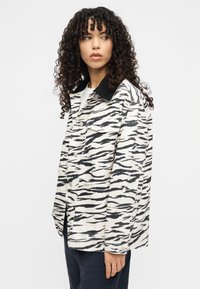 Μαύρο και άσπρο τζάκετ με ρίγες τύπου τίγρης, με γιακά, κλείσιμο με κουμπιά και δύο μπροστινές τσέπες, που παρουσιάζει υφή υφάσματος και casual σχεδιασμό.