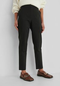 Svarta skräddarsydda byxor med hög midja, som har en mjuk tygyta och framfickor med detaljer. Kombinerat med bruna loafers med ormskinnstryck.