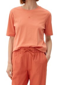 Koralfarvet bomulds t-shirt med korte ærmer og rund halsudskæring, med et lille broderet logo. Matchet med koralfarvede bukser med snoretræk.