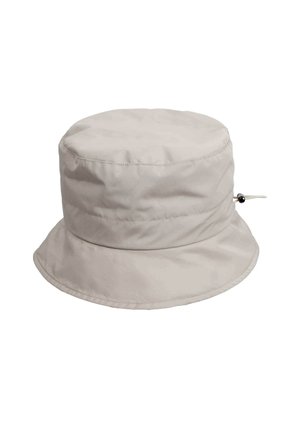 Beige bucket-hattu pehmeästä kankaasta, jossa on leveä lippa ja säädettävä nyöri, jossa on pyöreä helmi sivussa.