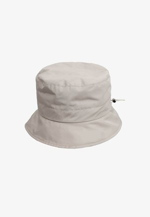 Beige bøttehat lavet af blødt stof, med en bred skygge og en justerbar snor med en cirkulær perle på siden.