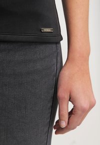 Černý fitted top s ribovanou texturou a vyšitou značkovou etiketou. Šedé džíny s mírným opotřebováním, zdůrazňující úzké přilnutí.