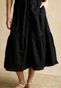 Schwarzes Baumwoll-Maxikleid mit einem strukturierten floralen Muster, Knopfverschluss und Taschen. Verfügt über einen gestuften Rock und eine fließende Silhouette.