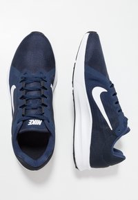 Baskets de sport bleu marine avec tige en mesh, swoosh blanc de Nike, semelle en caoutchouc noir et système de laçage ; dotées d'un col et d'une languette rembourrés.