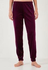 Velvet dark purple pajama pants with an elastic waistband and tapered ankles, featuring a smooth texture and two side pockets.