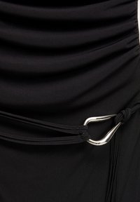 Vêtement en tissu noir avec une texture froncée et de fines bretelles noires passant à travers un anneau métallique argenté en forme de goutte sur le côté droit.