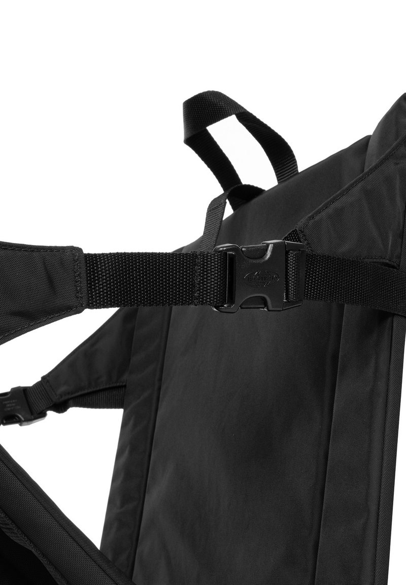 Mochila de tela negra con correas ajustables, herrajes de plástico en forma de hebilla y una textura suave con detalles de costura reforzada.