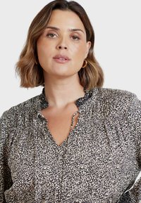 Svart och gräddfärgad blus med ett mönster, texturerad, smockad halsringning och en V-formad öppning. Har långa ärmar och en avslappnad passform.