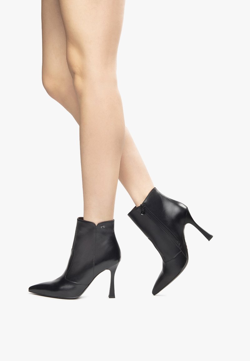 Bottes noires en cuir à la cheville avec des orteils pointus, de hauts talons aiguilles, des fermetures éclair sur le côté et une texture lisse.