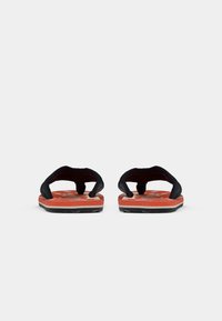 Pair of orange flip-flops with black straps and white floral patterns, viewed from the front on a plain white background.