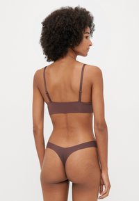 Conjunto de sujetador y tanga en marrón sin costuras, hecho de tejido suave, con tirantes ajustables y un diseño minimalista sin hardware visible.