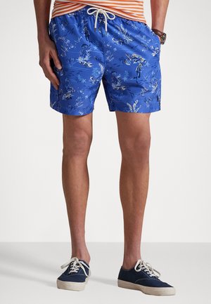Bermudas de banho azuis com um padrão floral, cintura elástica e cordão ajustável. Usadas com sapatos de lona azul-marinho.