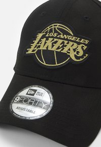 Gorra de béisbol negra con el logo dorado de "Los Angeles Lakers", visera curva y etiqueta ajustable New Era 9FORTY. La textura del tejido es suave.