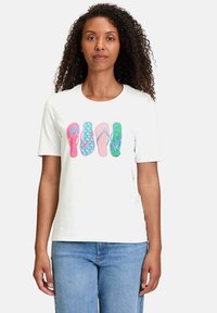 T-shirt blanc avec des motifs de tongs colorés en rose, bleu, vert et violet. Manches courtes et encolure ronde.