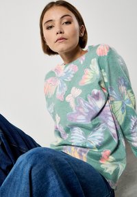 Sweter dzianinowy w miętowym kolorze z wielokolorowymi wzorami motyli i dekoracyjnym przeszyciem. Połączony z dżinsami, tkanina o teksturze.