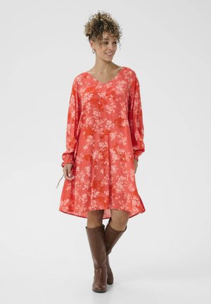 Ziedu raksta sarkana kleita ar V-veida kakla izgriezumu, garām piedurknēm un brīvu piegriezumu, saskaņota ar brūnām ceļgala augstām zābakām. Daiļš, viegls audums.