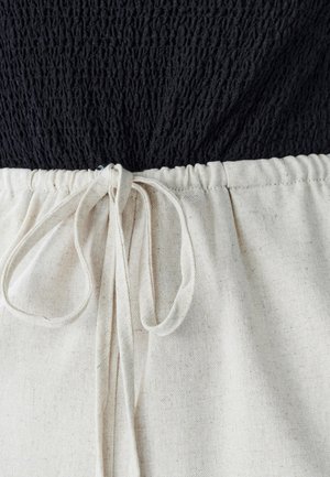 Mustvalge smockkangas ülemises osas üleminek kreemika tekstuuriga kangale alumises osas, millel on kokkuköitmiseks keeratud sõlmedega pael.