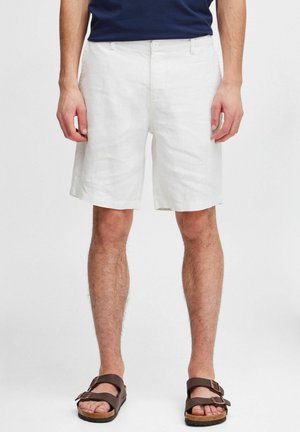 White linen shorts with a relaxed fit, featuring a flat front, side pockets, and a smooth texture. Paired with brown sandals.