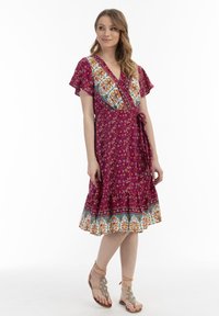 Rochie wrap în magenta cu imprimeu floral și accente albastre, având mâneci fluture, talie legată și detalii cu volane la tiv.