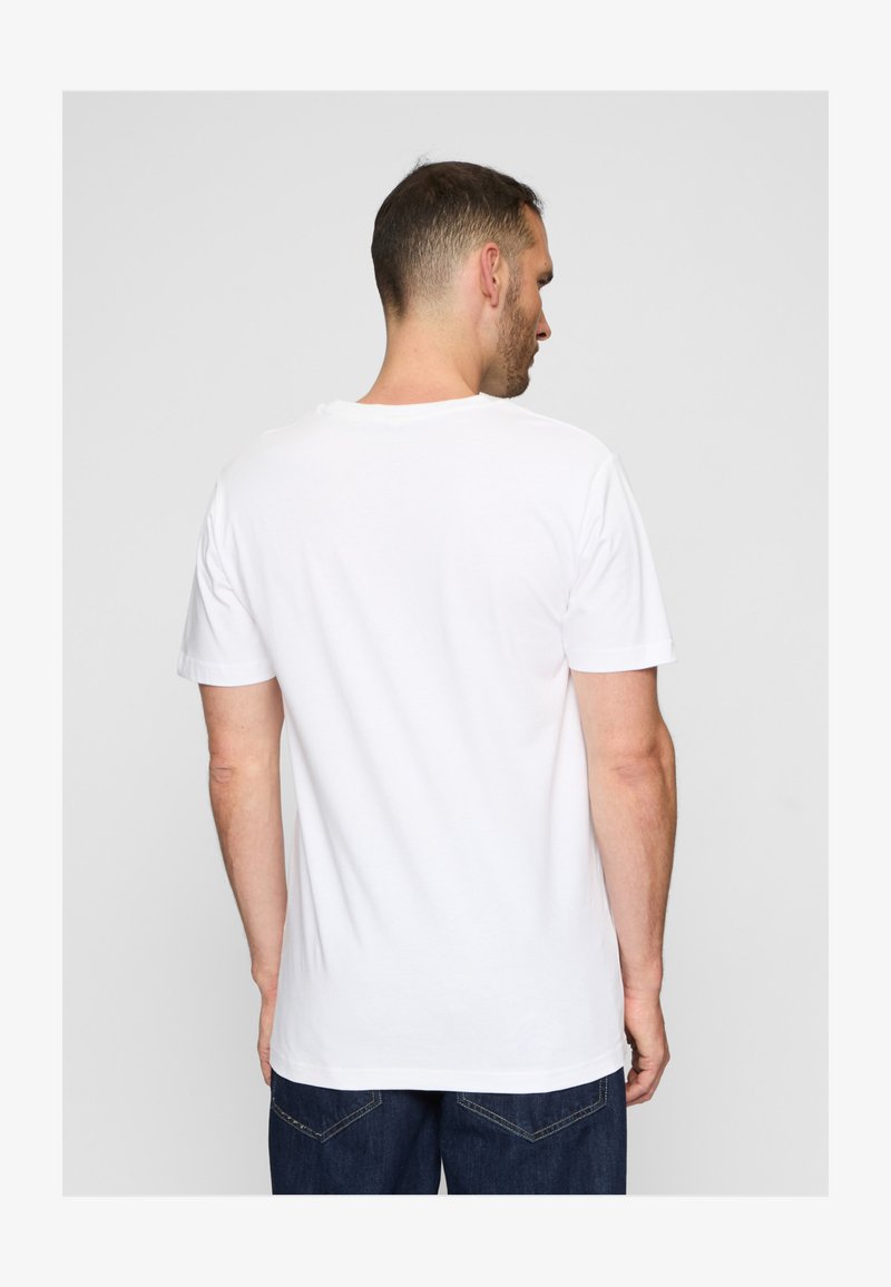 Mand iført en ensfarvet hvid kortærmet t-shirt og mørkeblå jeans, vist bagfra mod en ensartet lysegrå baggrund.