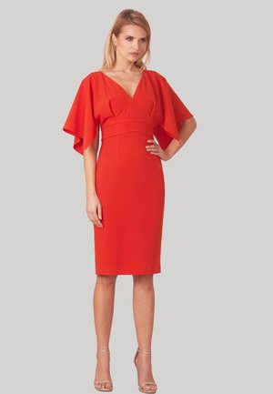 Czerwona sukienka z dekoltem w kształcie litery V i szerokimi, falującymi rękawami, dopasowana w talii, do kolan, wykonana z gładkiego materiału; zestawiona z przezroczystymi sandałami.