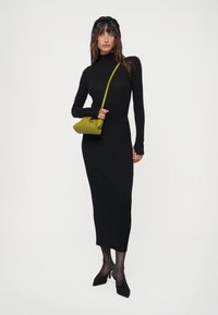 Melna garās piedurknes turtlenecks blūze un ribota melna midi svārki. Izskatu papildina maza austs zaļa roku soma ar garu siksnu.