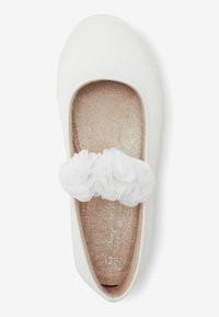 Bailarinas blancas con un upper de tela suave, decoradas con una tira de tul blanco en forma de flor y una plantilla brillante en color beige. Diseño de punta redonda.