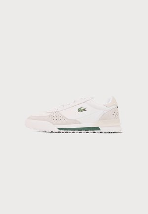 Witte en beige sneaker met groene accenten en een groen krokodillenlogo aan de zijkant, getoond vanaf de buitenkant tegen een lichte achtergrond.