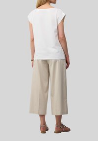 Witte korte mouw top met een brede halslijn, gecombineerd met lichte beige wijde broekspijpen, gedragen met zilveren enkelsandalen met bandjes.